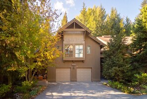 Une maison à deux étages avec un garage, entourée d’arbres et dotée d’une allée.