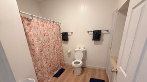 A bathroom with a toilet, a shower curtain, a towel rack, and a floor mat. - Beautiful 2-bedroom apartment with AC in charming Hutchinson (Hutchinson)