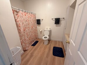 Ein Badezimmer mit Toilette, Duschvorhang, Handtuchhalter und Fußmatte.