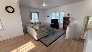 A living room with a sofa, a television, a rug, and a staircase.