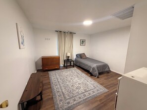 Allotjament petit i d'una sola habitació amb un llit, un taulell de fusta, una taula petita, una làmpada, una catifes i un armari blanc.