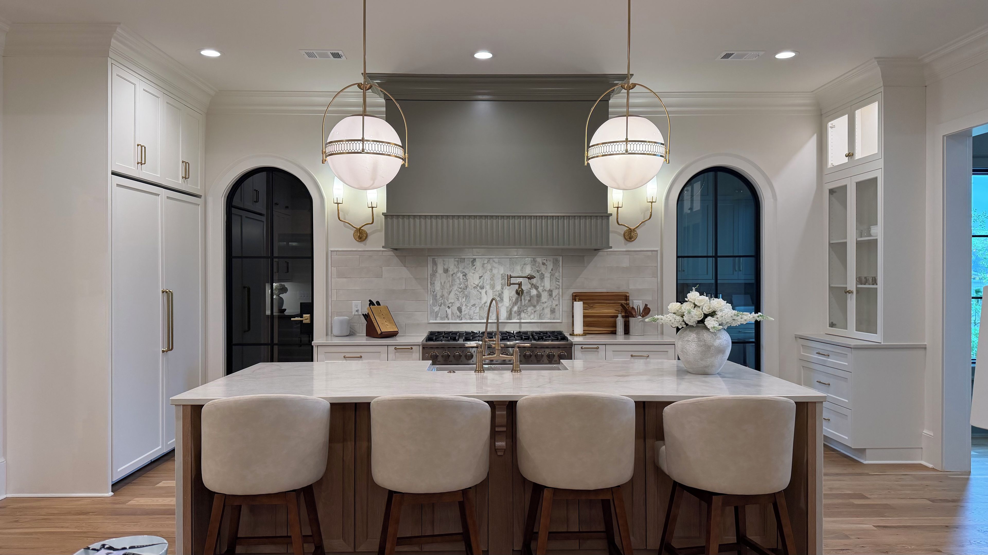 A kitchen with a large island, bar stools, a gas stove, and pendant lighting.