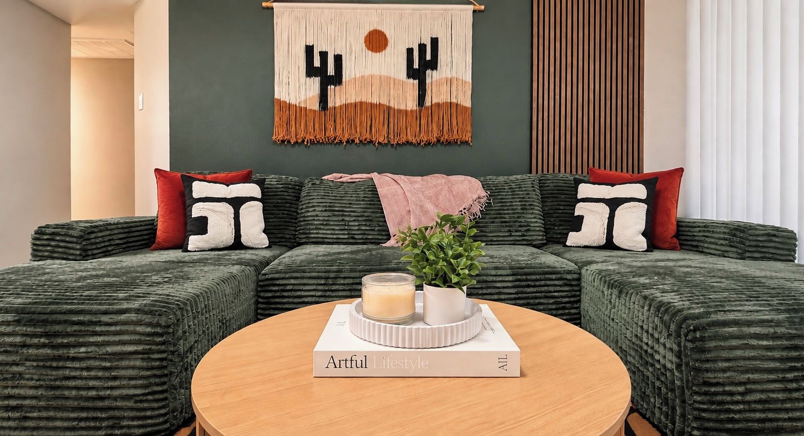 A green upholstered sofa with a book titled 'Artful Lifestyle' on a round wooden table.