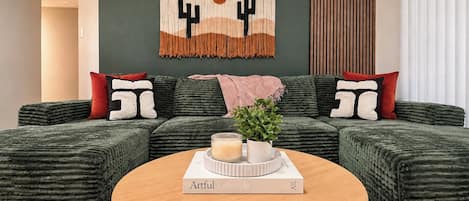 A green upholstered sofa with a book titled 'Artful Lifestyle' on a round wooden table.