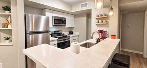 A modern kitchen with stainless steel appliances, a white countertop, and a built-in oven. - Near ASU • King Bed • Arcade • Pool/Spa • Sleeps 8 • Pets • 65" TV • W/D (Tempe)