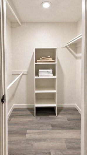 A walk-in closet with a white shelving unit, grey wooden flooring, and a white door. - Near ASU • King Bed • Arcade • Pool/Spa • Sleeps 8 • Pets • 65" TV • W/D (Tempe)