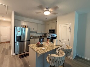 Una cocina moderna con un refrigerador de acero inoxidable, encimera de granito y ventilador de techo.