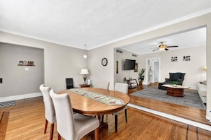 A dining area with a wooden table and chairs, a rug, a lamp, and a ceiling fan.