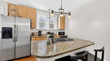 Cocina moderna con refrigerador de acero inoxidable, encimera de granito, armarios de madera y microondas integrado.