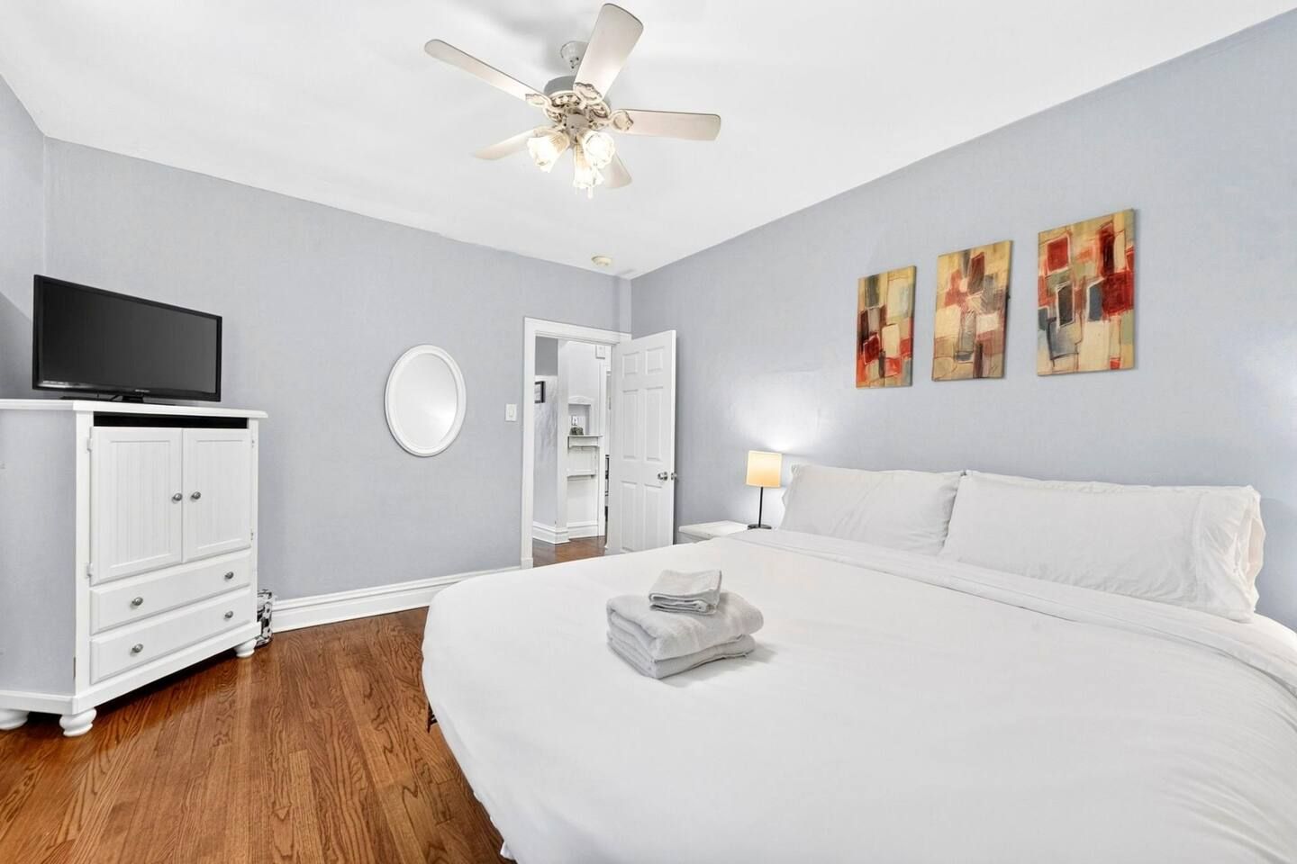 Habitación de hotel con cama, televisión, armario, ventilador de techo y obras de arte en la pared.
