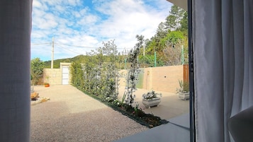 Vista a través de una ventana que muestra una zona residencial con un camino pavimentado, una cerca de madera y una puerta que da a una casa.