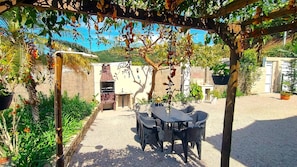 Un patio exterior con una parrilla de ladrillo, una mesa y sillas, y plantas en macetas.