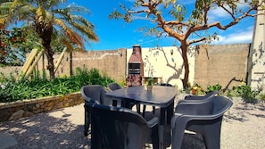 Un patio al aire libre con una mesa y sillas, rodeado de plantas y un muro de ladrillo.