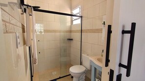 Un baño con cabina de ducha de vidrio, un inodoro y un lavamanos.