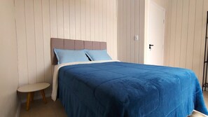 Una cama con cabecera, una mesita de noche y una puerta en una habitación con paneles verticales.
