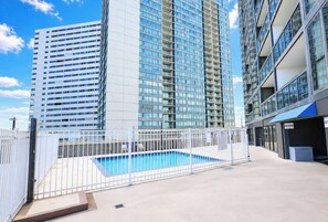 A rooftop swimming pool with a white fence, surrounded by high-rise buildings. - Golden Sands 1617 (Ocean City)