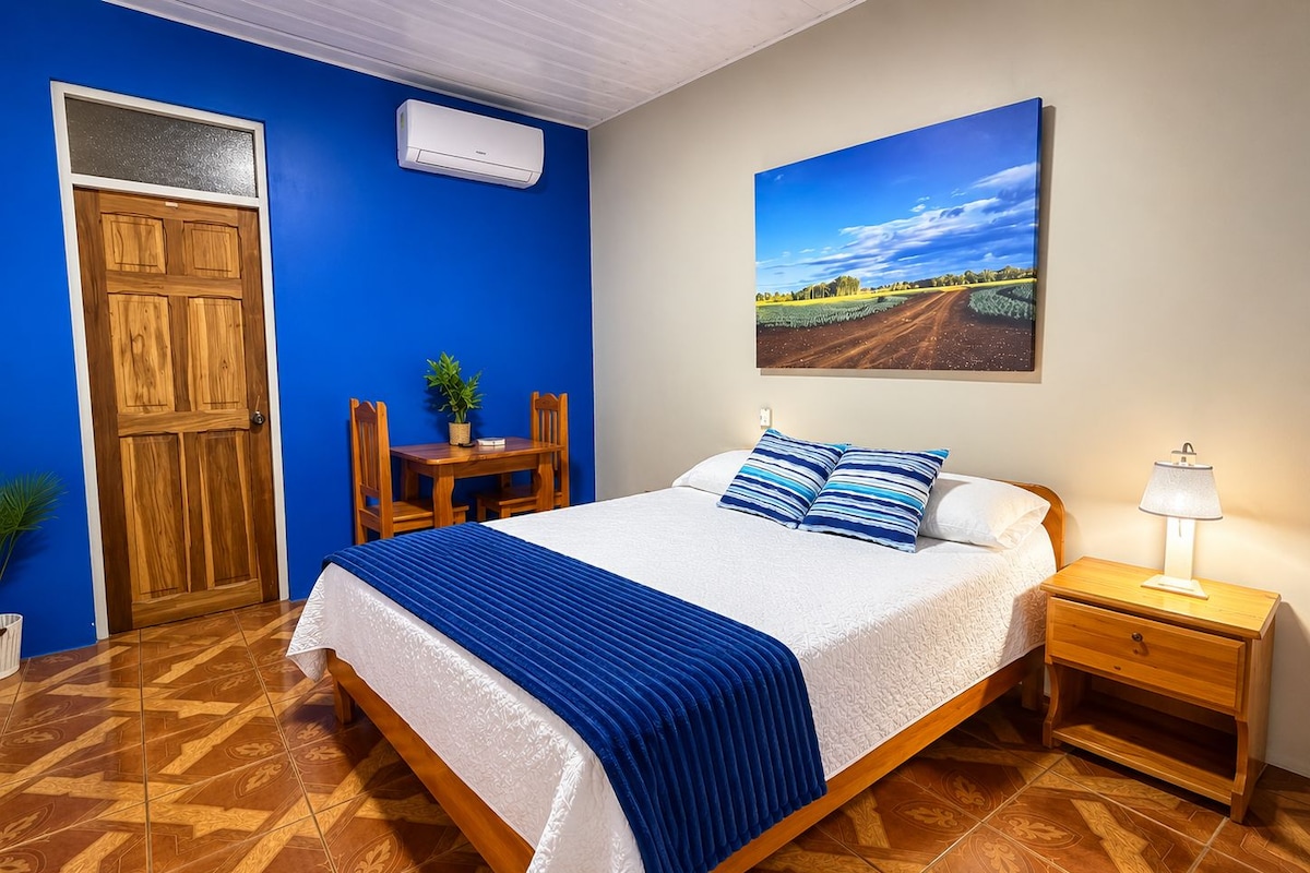 A bedroom with a bed, bedside table, lamp, and a painting on the wall.