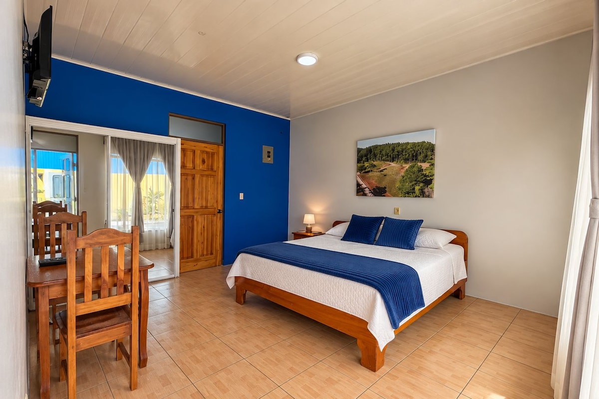 Ein Schlafzimmer mit einem Bett, einem Schreibtisch mit Stuhl, einem Fenster mit Vorhängen und einem Gemälde an der Wand.