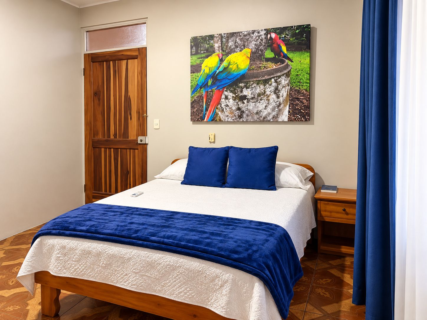 Ein Schlafzimmer mit einem Bett, einem Nachttisch, einer Holztür und einem Gemälde bunter Vögel.