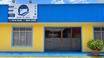 A hotel entrance with a blue and yellow facade, a reception desk, and a potted plant.