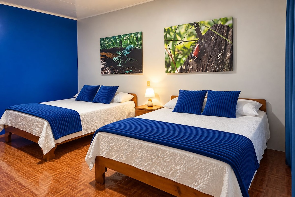 Ein Hotelzimmer mit zwei Betten, jeweils mit blauer Bettdecke und weißen Laken, Holz-Kopfteilen und einem Nachttisch mit Lampe.