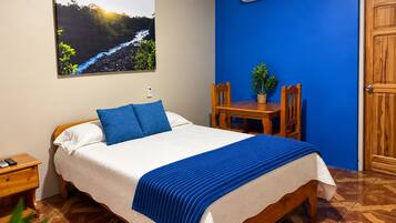 A bedroom with a bed, a nightstand, a table with chairs, a potted plant, and an air conditioning unit.