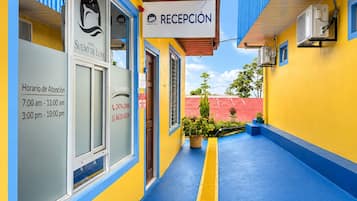 Zona de recepción de un hotel con mostrador, ventanal con vista al cielo y cartel con el nombre del hotel y horario de atención.