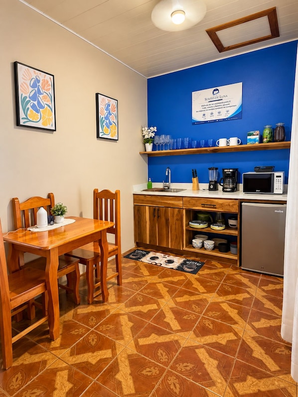 A compact kitchen with a dining area, featuring a microwave, coffee maker, and a refrigerator.