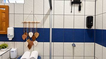 A bathroom with a blue and white tiled wall, a shower, a toilet with two towels, a soap dispenser, and a hanging decorative item.