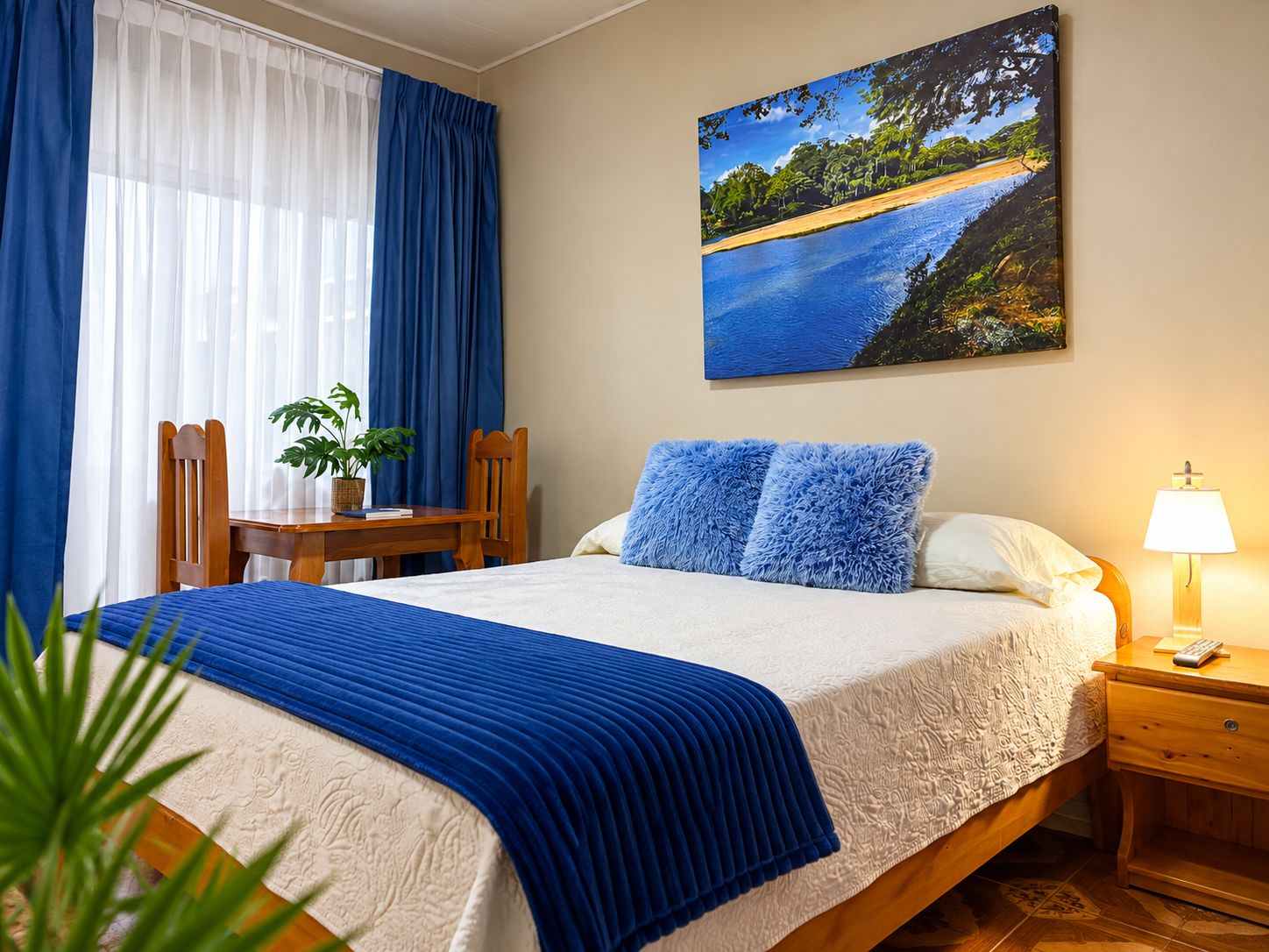 Un dormitorio con cama, escritorio, silla, lámpara y un cuadro en la pared.