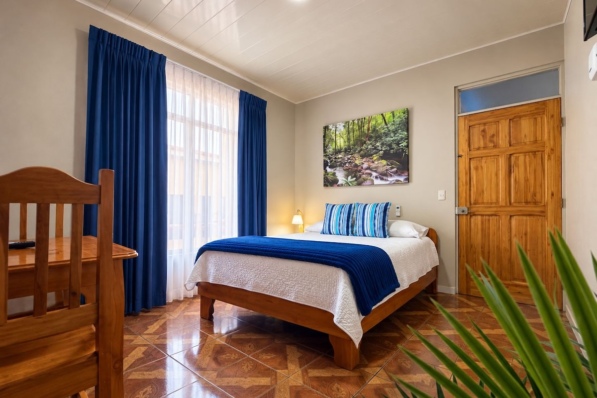 Ein Schlafzimmer mit einem Bett, einem Sessel, einem Gemälde und einer Tür.