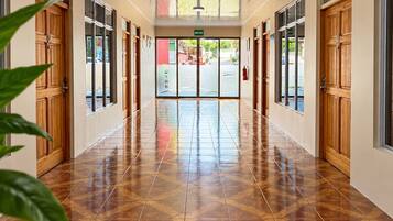 Un pasillo con puertas de madera y piso de baldosas, que conduce a una entrada con puertas de cristal.