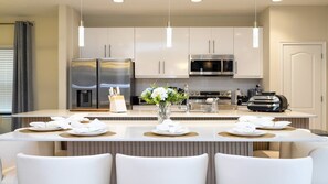 A modern kitchen with stainless steel appliances, a central island with seating, and a vase of flowers. - Cozy 6BR Balmoral Retreat, Pool, Spa & Waterpark (Haines City)