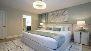 Une chambre à coucher avec un grand lit, deux tables de chevet avec des lampes, un lustre et un tableau au mur.