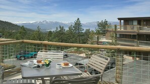 Un balcone con un tavolo apparecchiato per due persone, affaccia su un paesaggio montuoso con vette innevate e un lago.