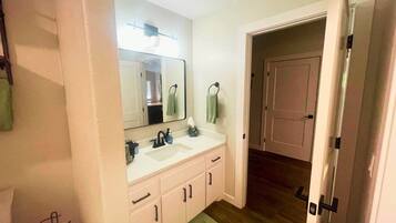 Un baño con lavamanos doble, un espejo y una puerta que da a otra habitación.