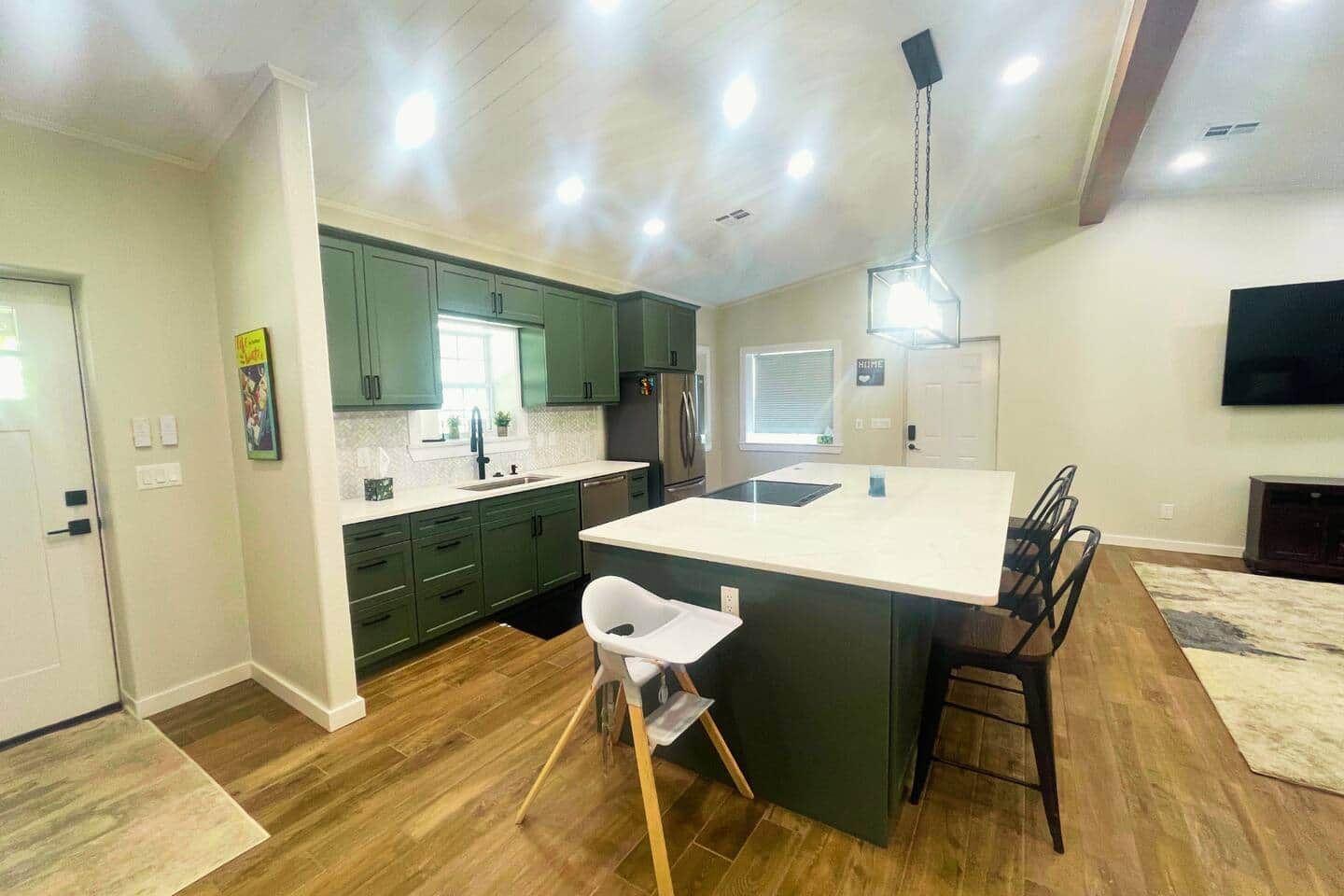 Een moderne keuken met een centraal eiland, donkergroene kasten en een wit aanrecht.
