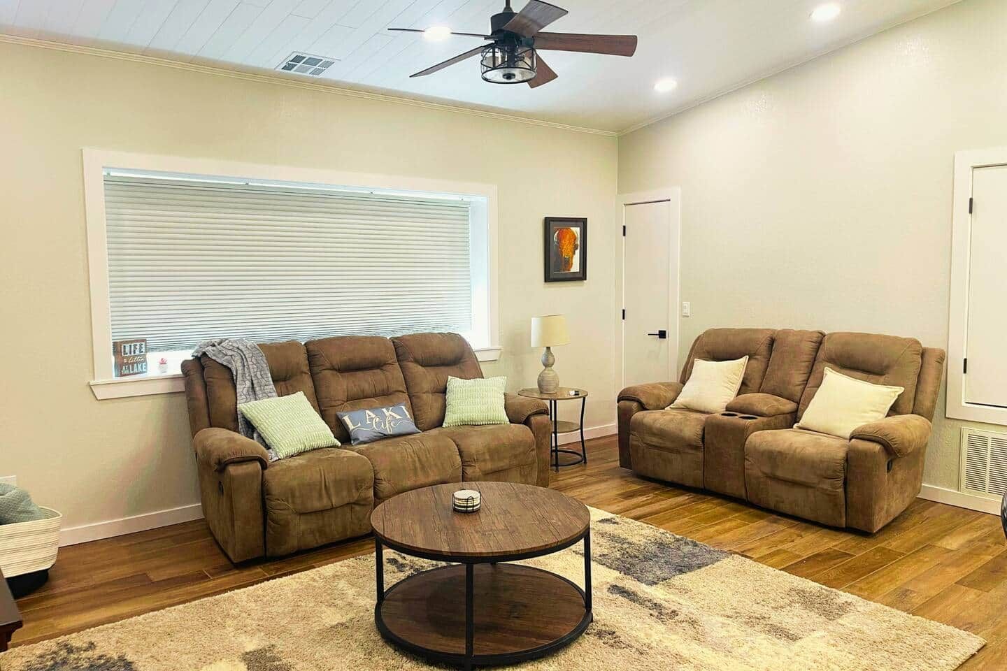 A living room with two brown sofas, a round coffee table, and a ceiling fan.