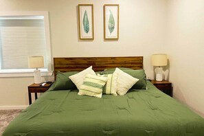 A bedroom with a wooden headboard, green bedding, two bedside lamps, and two framed leaf artworks on the wall.
