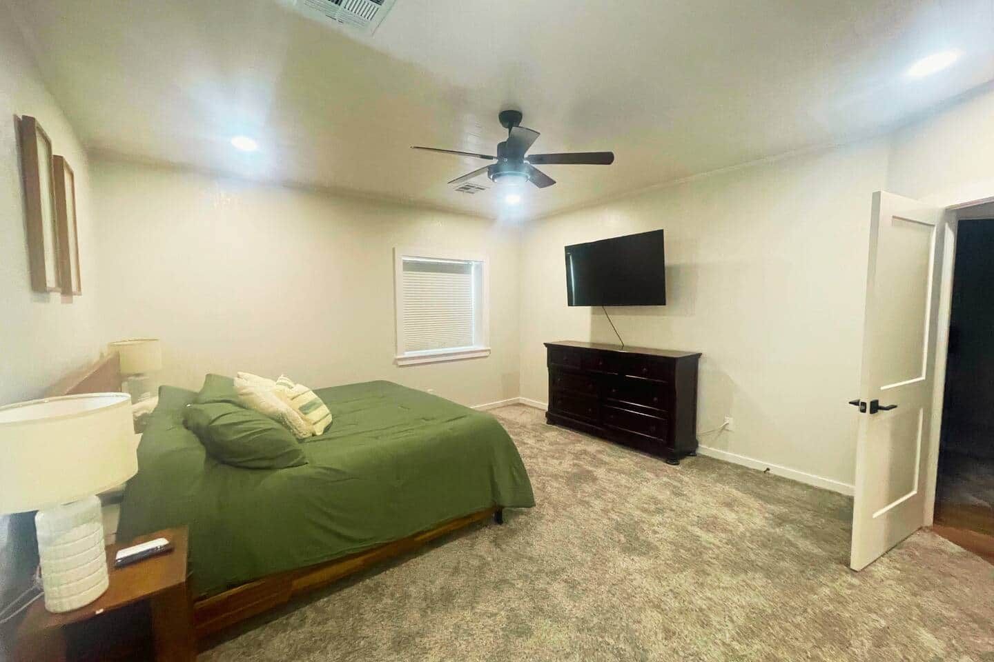 Un dormitorio con cama, cómoda, televisor, ventilador de techo y una puerta.