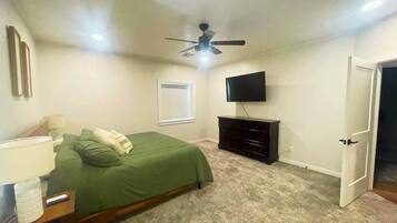 Un dormitorio con cama, cómoda, televisor, ventilador de techo y una puerta.