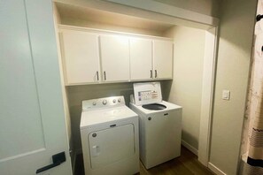 A laundry room with a washer and dryer, white cabinets above, and a door to the right.