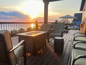 A deck with outdoor furniture, a table, and a view of the sunset over the water. - Sunset Point: Waterfront Home w/ amazing lake views, large deck, and hot tub! (Texanna)