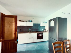 Uma cozinha compacta com armários brancos, uma pia de aço inoxidável e uma geladeira preta.