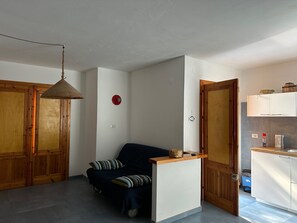 A compact living space with a sofa, a small table, a hanging light fixture, and wooden doors. - Scopello, direct access to the sea (Sicilia)