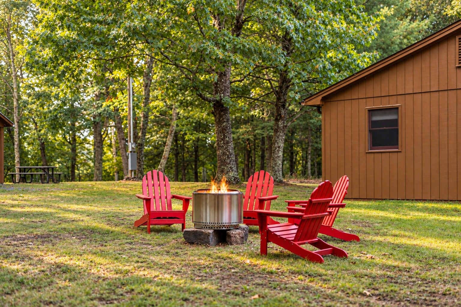 Eine Holzhütte mit Lagerfeuerstelle und roten Adirondack-Stühlen in einem bewaldeten Gebiet.