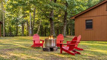 Eine Holzhütte mit Lagerfeuerstelle und roten Adirondack-Stühlen in einem bewaldeten Gebiet.