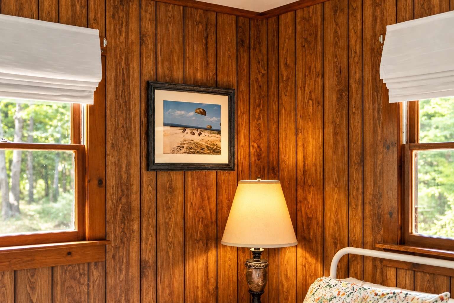 Ein Zimmer mit Holzwandverkleidung, einem gerahmten Bild, einer Lampe und einem Bett.
