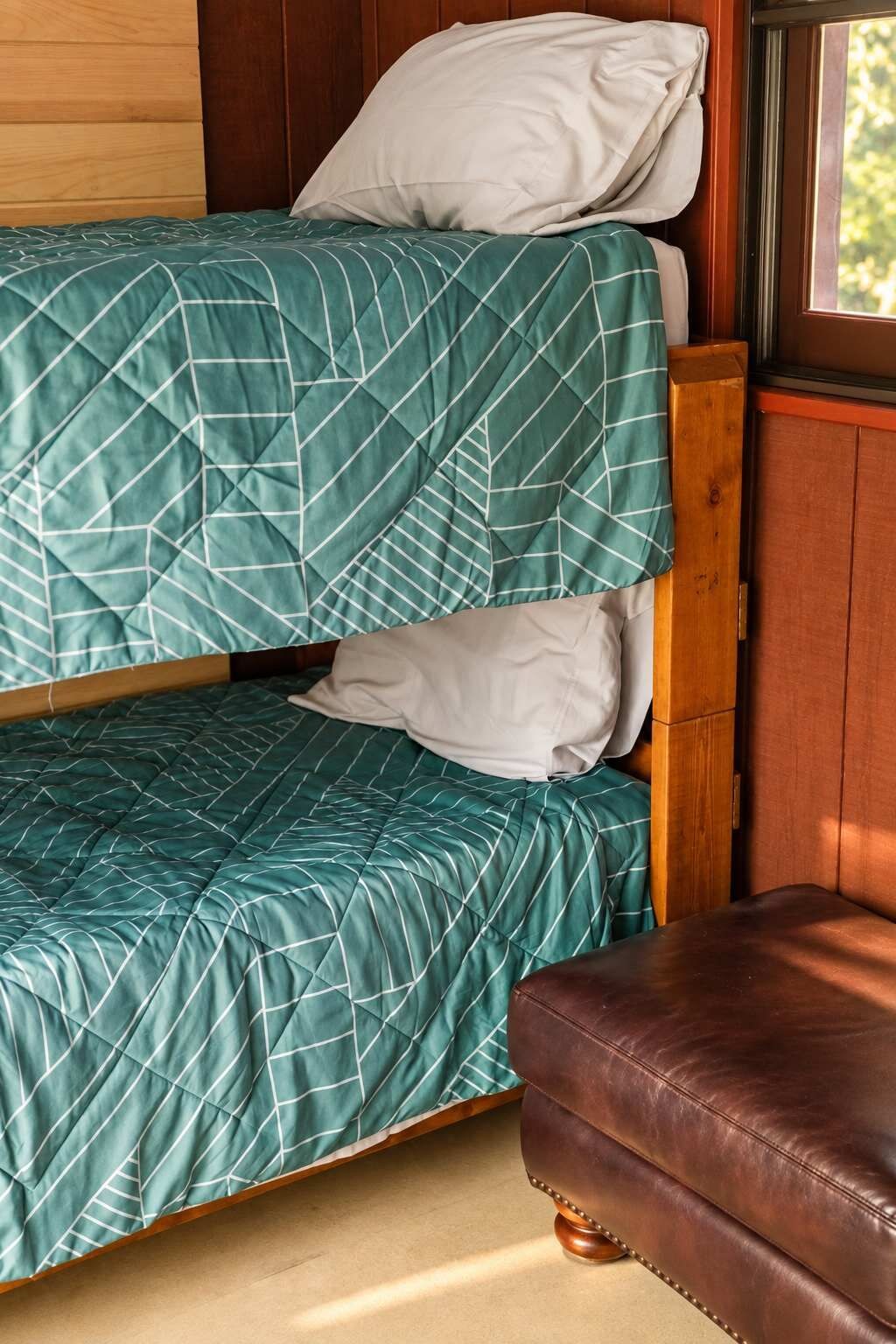 Un lit superposé avec une couvre-lit à motifs géométriques, une tête de lit en bois et un banc en cuir.