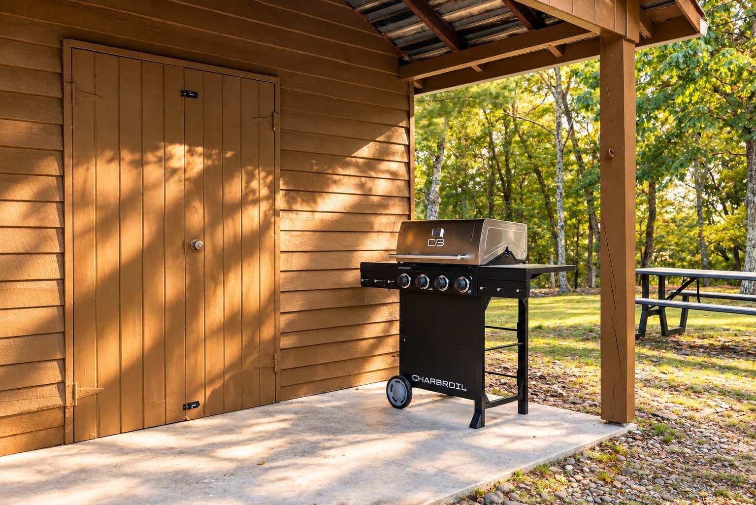 Ein Grill mit Rädern, eine überdachte Terrasse und ein Holzgebäude im Hintergrund.